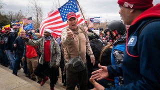 WASHINGTON, DC - JANUARY 06: Ray Epps, in the red Trump hat, center, gestures to others as people gather on the West Front of the U.S. Capitol on Wednesday, Jan. 6, 2021 in Washington, DC. January 6 marks the second day of Pro-Trump events fueled by President Donald Trump's continued claims of election fraud in an to overturn the results before Congress finalizes them in a joint session of the 117th Congress.