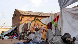 Men sit and lie outside tents and shelters pitched at the Hasahisa secondary school on July 10, 2023, which has been made into a make-shift camp to house the internally displaced fleeing violence in war-torn Sudan. Conflict-torn Sudan is on the brink of a “full-scale civil war” that could destabilise the entire region, the United Nations warned on July 9, after an air strike on a residential area killed around two dozen civilians.