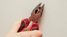 Close up view of person hand removing old plastic dowel, nylon wall plug from drywall with pliers at home. Home renovations concept.