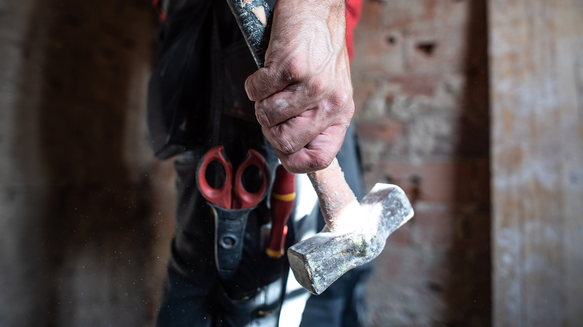 A hand holding a hammer against a steel background.