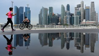TOPSHOT – People pass by as the city skyline is reflected in a puddle leftover from earlier rain in Singapore on February 8, 2022. (Photo by Roslan RAHMAN / AFP) (Photo by ROSLAN RAHMAN/AFP via Getty Images)