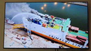 A photo displayed on a video monitor in Union,N.J., Wednesday, Jan. 10, 2024 shows a burning cargo ship in Newark N.J. on July 5, 2023. Federal investigators are conducting hearings into the blaze that killed two Newark, N.J. fire captains.
