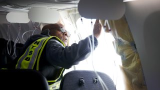 In this National Transportation Safety Board (NTSB) handout, NTSB Investigator-in-Charge John Lovell examines the fuselage plug area of Alaska Airlines Flight 1282 Boeing 737-9 MAX on Jan. 7, 2024 in Portland, Oregon.