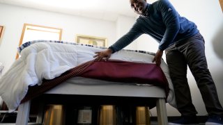Seth Robinson, a chiropractor who serves as Tesla BioHealing's medical director, lifts bed skirts to show "biohealers" – canisters that the company claims exude "life force energy," or biophotons, at the Tesla BioHealing & MedBed Center, in Milford, Del., Tuesday, Oct. 3, 2023.