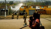 A woman evacuates with her dog as firefighters conduct a protective water spray on homes as forest fires burn nearby, in Vina del Mar, Chile, Saturday, Feb. 3, 2024. Officials say intense forest fires burning around a densely populated area of central Chile have left several people dead and destroyed hundreds of homes. (AP Photo/Esteban Felix)