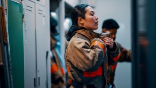 Female firefighter putting on her protective equipment inside the fire station in response to an emergency