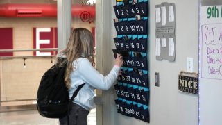 A ninth grader places her cellphone in to a phone holder as she enters class