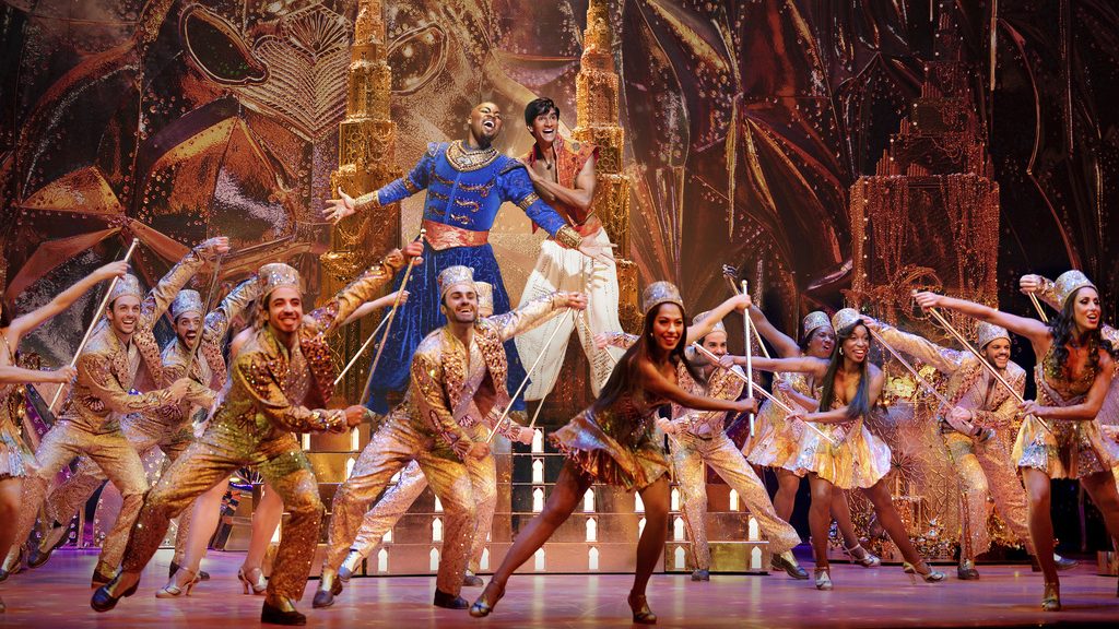 This image released by Disney Theatricals shows Michael James Scott as Genie, background left, and Michael Maliakel as Aladdin, background right, during a performance of "Aladdin on Broadway." (Matthew Murphy/Disney Theatricals via AP)