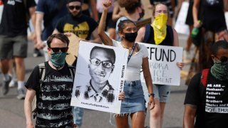 FILE - Demonstrators carry placards during a rally and march over the death of Elijah McClain in Aurora, Colo., June 27, 2020.