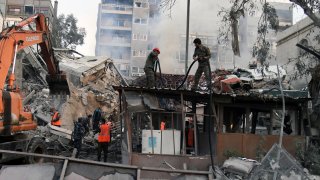 In this photo released by the official Syrian state news agency SANA, emergency service workers clear the rubble at a destroyed building struck by Israeli jets