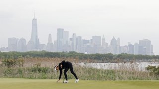 Nelly Korda places her golf ball on the green at Liberty National Golf Club in Jersey City and the New York City skyline can be seen in the background.