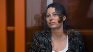 Ksenia Karelina sits in a glass cage in a court room.