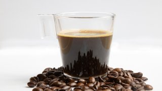 A glass coffee mug with a shot of espresso in the cup next to raw organic Arabica variety coffee beans on white background isolated.