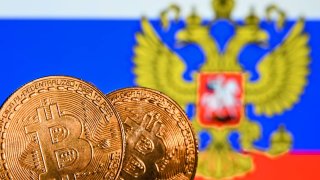 Illustrative image of two commemorative bitcoins seen in front of the national flag of Russia displayed on a computer screen.