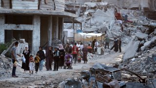 Palestinians displaced by the Israeli air and ground offensive on the Gaza Strip walk next to sewage flowing into the streets