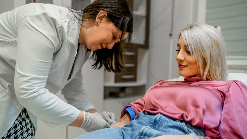 Nurse drawing blood from a female patient's arm vein in the medical clinic