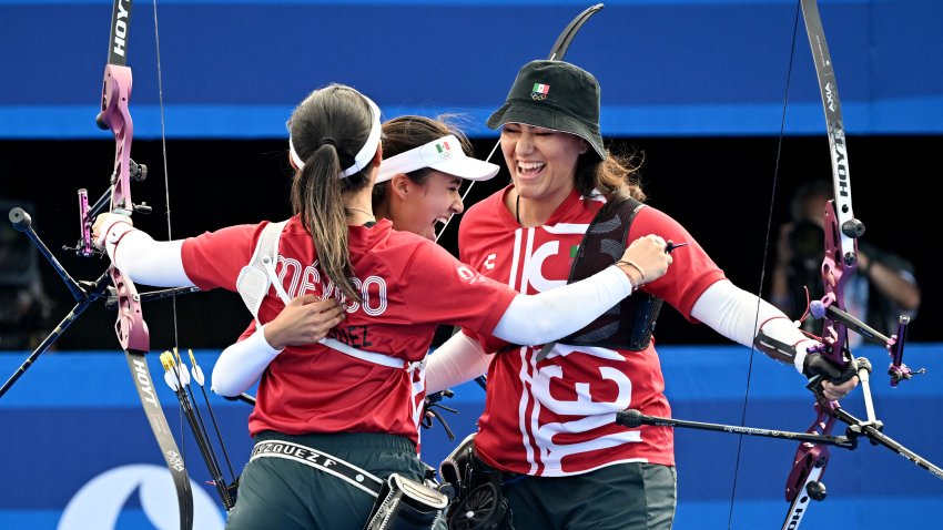 3 integrantes femeninas del Equipo México de tiro con arco celebran la victoria, sosteniendo arcos y abrazándose.