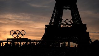 Spectators watch a quarterfinal beach volleyball match between Australia and Switzerland at sunset at Eiffel Tower Stadium at the 2024 Summer Olympics, Tuesday, Aug. 6, 2024, in Paris, France. (AP Photo/Robert F. Bukaty)