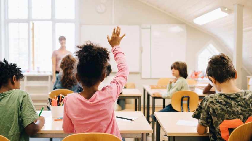 Rear view of boy raising hand while answering in class at elementary school