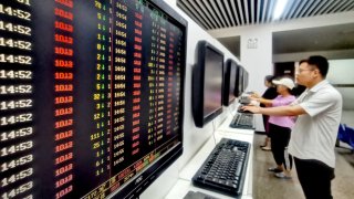 Investors watch computer screens displaying stock price figures at a stock exchange hall.