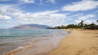 Pedestrians walk along a beach in Kihei, Maui County, Hawaii