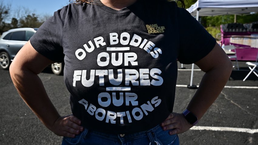 A woman poses for pictures wearing a shirt that reads "Our bodies, our futures, our abortions."