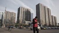 A pedestrian crosses a road in front of residential buildings in Beijing, China.