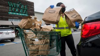 An independent contractor wearing a protective mask and gloves loads Amazon Prime grocery bags into a car outside a Whole Foods Market in Berkeley, California, on October 7, 2020.