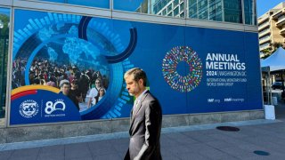 A man walks past signage for the the 2024 IMF/World Bank Annual Meetings outside of the headquarters of the International Monetary Fund in Washington, DC on October 18, 2024. 