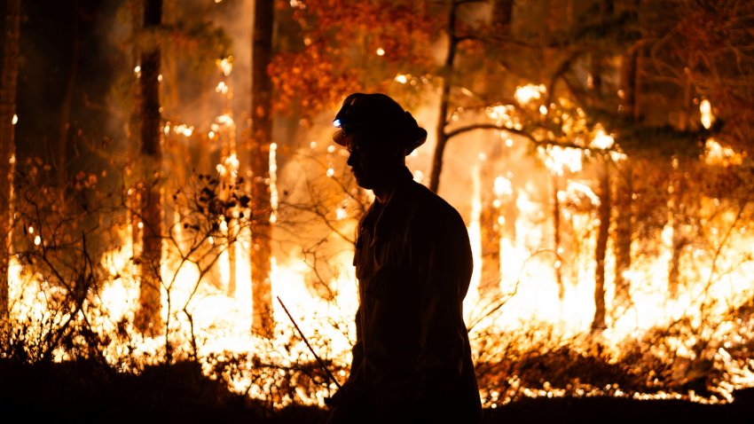 a firefighter is silhouetted against a forest fire