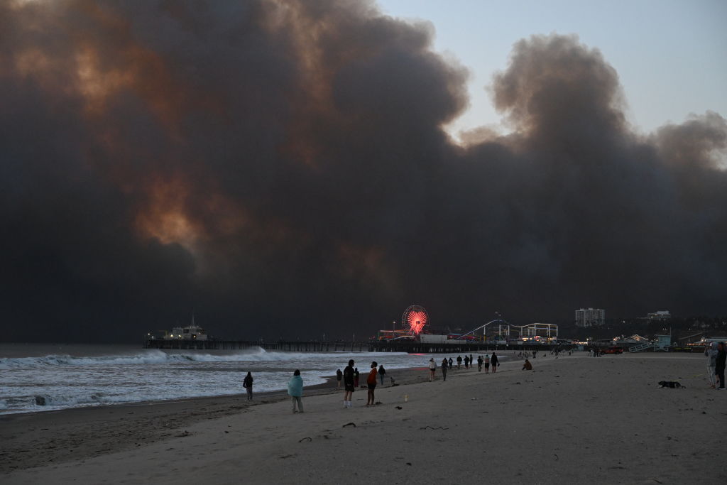 Smoke from the Palisades Fire fills the sky as seen from Santa Monica Beach, with the Santa Monica Pier and Ferris Wheel in the foreground on Jan. 7, 2025.