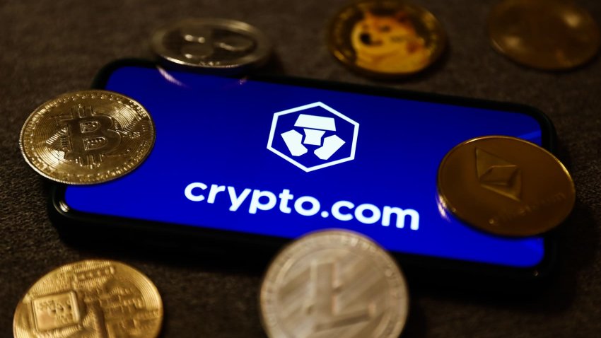 Crypto.com logo displayed on a phone screen with representation of cryptocurrencies.