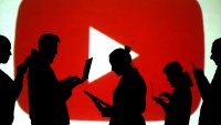 Silhouettes of laptop and mobile device users are seen next to a screen projection of the YouTube logo.