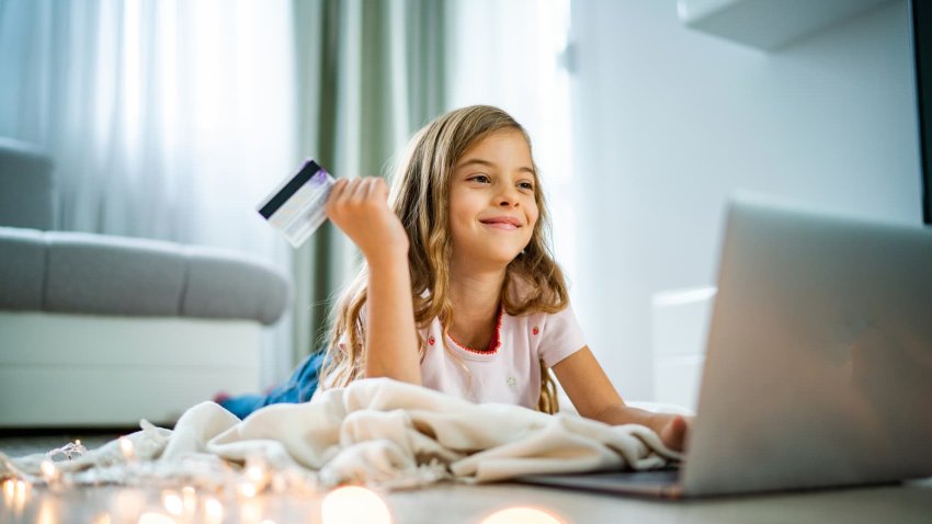 Smiling teen girl holds credit card and searching what to buy online