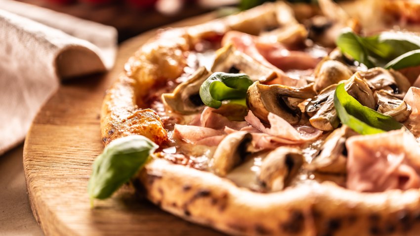 Pizza baked with mushrooms and ham with fresh basil on top.