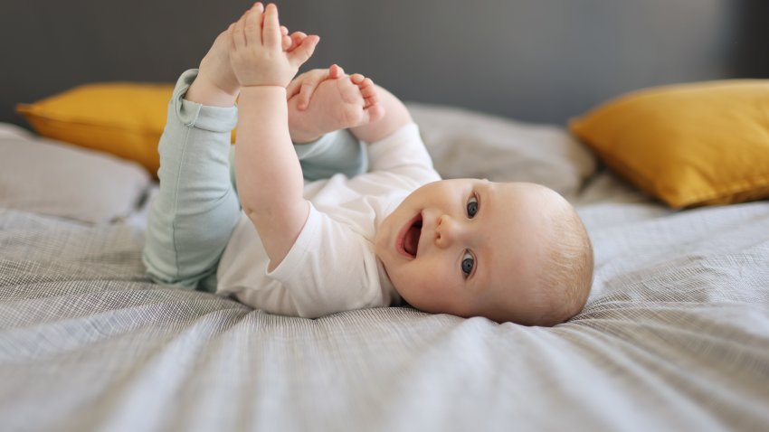 A baby boy smiling, laying on a bed